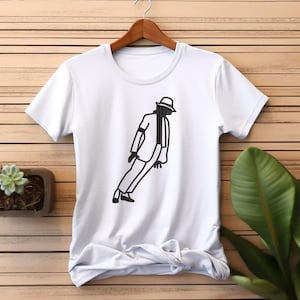 May include: White t-shirt with a black outline illustration of a person in a suit, hat, and shoes, in a dancing pose. The design is centered on the front of the shirt. The shirt is hanging on a wooden hanger.
