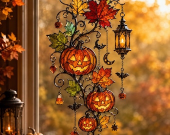 Puede incluir: Una decoración colgante de vitral con tres calabazas iluminadas, hojas de arce otoñales en rojo, naranja y verde, una pequeña linterna, murciélagos, una luna creciente y un dije de caramelo, todo unido por un marco de metal negro.