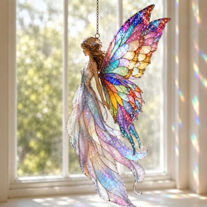 May include: A hanging ornament featuring a fairy figure with large, iridescent, multi-coloured wings in shades of blue, purple, yellow, and red. The fairy wears a flowing, translucent gown with shimmering details, suspended by a metal chain.