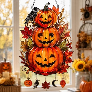 Peut inclure: Un attrape-soleil en vitrail représentant trois citrouilles d'Halloween orange empilées avec des visages sculptés, entourées de feuilles d'automne et d'épis de blé. Un corbeau noir est posé sur les citrouilles, avec des breloques suspendues.