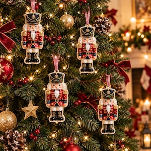Puede incluir: Cuatro adornos idénticos de cascanueces colgados de un árbol de Navidad. Cada cascanueces lleva un sombrero negro con una estrella dorada, una chaqueta roja con adornos dorados, pantalones azules y botas negras, suspendidos por una cinta de cuadros rojos y blancos.