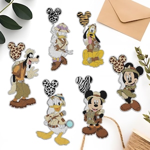 May include: Six embroidered iron-on patches featuring Disney characters dressed in safari outfits. The characters include Mickey Mouse, Minnie Mouse, Donald Duck, Goofy, and two versions of Pluto. Each character is holding a balloon with an animal print design.