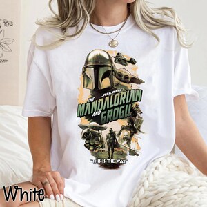 Puede incluir: Camiseta blanca con un dise&ntilde;o gr&aacute;fico de la serie Star Wars, "The Mandalorian and Grogu". El dise&ntilde;o incluye el casco mandaloriano, Grogu y la frase "This is the Way".