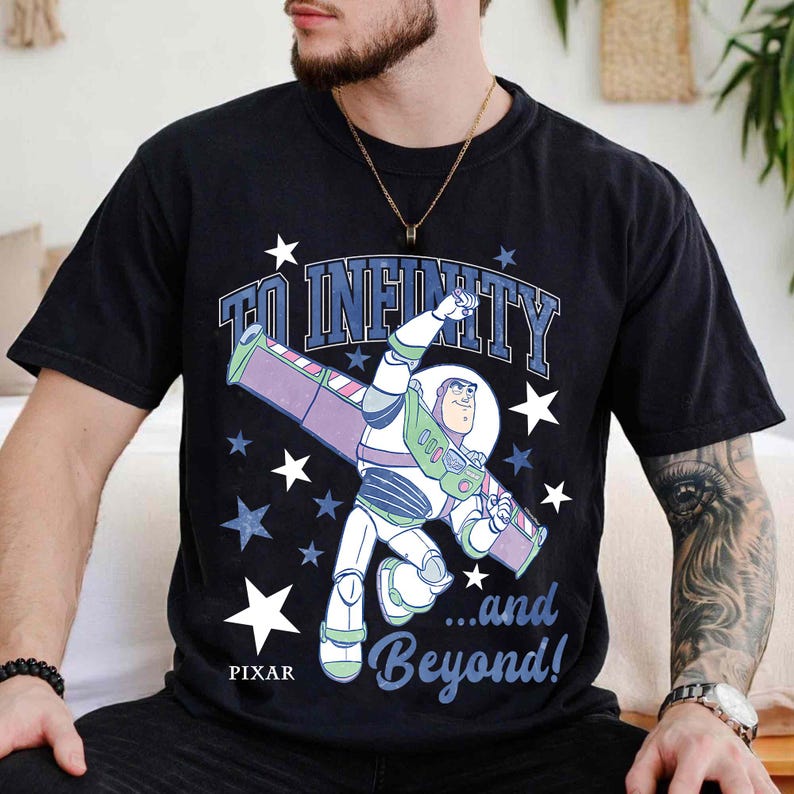 Puede incluir: Camiseta negra con Buzz Lightyear de Toy Story de Pixar. El dise&ntilde;o incluye la frase "TO INFINITY...and Beyond!" con gr&aacute;ficos de estrellas. La camiseta tiene cuello redondo y mangas cortas.