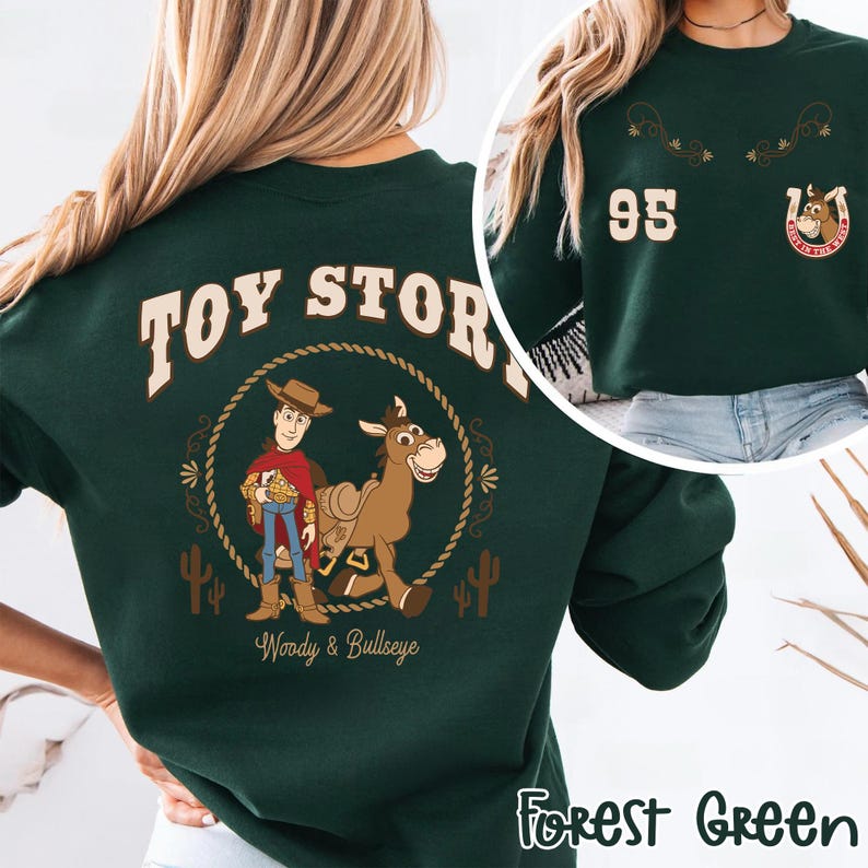 May include: Forest green sweatshirt featuring a graphic of Woody and Bullseye from Toy Story, with the text "TOY STORY" above the characters. The sweatshirt also has the number "95" and a horseshoe graphic on the upper right.