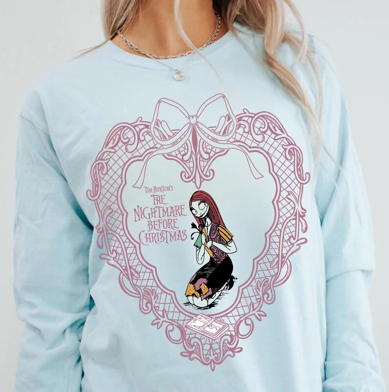 May include: Pale blue long-sleeved top with a pink heart-shaped design, a bow, and the text "Tim Burton's The Nightmare Before Christmas." The design features an illustration of Sally from the film.