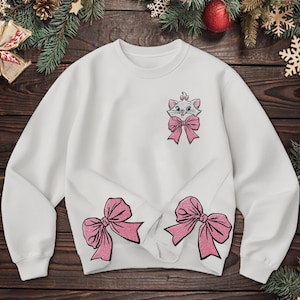 May include: White sweatshirt featuring an embroidered image of a cat with a pink bow, and two large pink bows at the bottom. The sweatshirt is a crew neck style, perfect for casual wear.