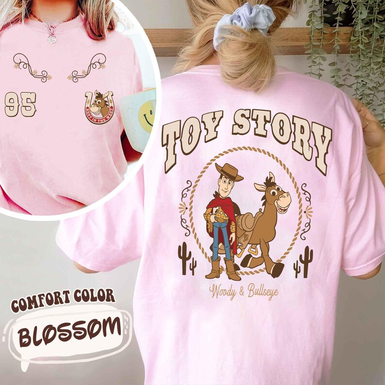 May include: A light pink t-shirt with the text "TOY STORY" on the back, featuring Woody and Bullseye. The front has the number "95" and a horseshoe graphic. The shirt is labeled "Comfort Color Blossom".