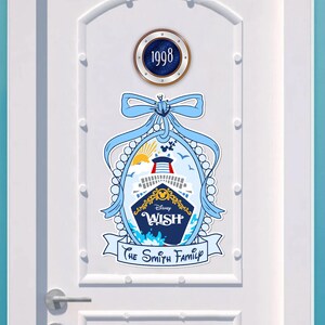 May include: A white door with a blue and gold Disney Wish cruise ship decal. The decal features a pearl necklace, a blue bow, and the text "Disney Wish" and "The Smith Family". A round porthole with the number "1998" is above the decal.