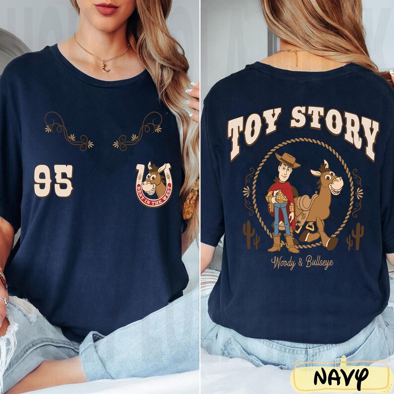 May include: Navy blue t-shirt featuring graphics from the movie Toy Story. The front displays the number 95, a horseshoe with a horse, and text. The back has the words "TOY STORY" above an image of Woody and Bullseye. The word "NAVY" is at the bottom.