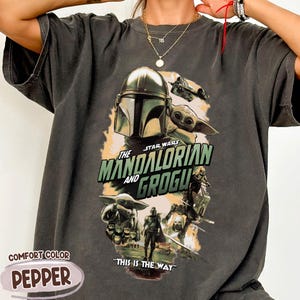 Puede incluir: Camiseta gris oscuro con un gr&aacute;fico de la serie Star Wars, "The Mandalorian and Grogu". El dise&ntilde;o incluye el casco del Mandaloriano, Grogu y el texto "THIS IS THE WAY". La camiseta est&aacute; etiquetada como "COMFORT COLOR PEPPER".