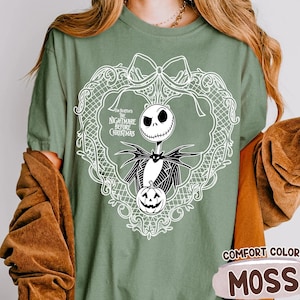 May include: Moss green t-shirt with a white graphic of Jack Skellington from "The Nightmare Before Christmas" in a decorative frame. The shirt also has the words "Comfort Color" and "Moss" printed on it.