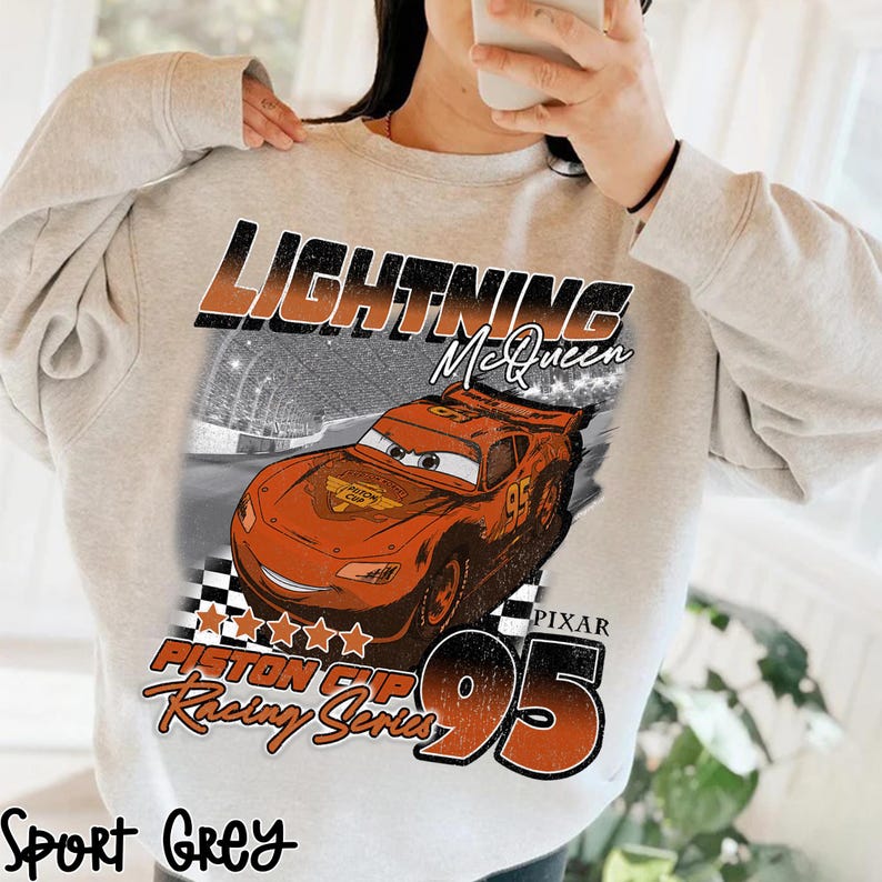 May include: Sport grey sweatshirt featuring a graphic of Lightning McQueen from the movie Cars. The design includes the text "Lightning McQueen", "Piston Cup Racing Series", and the number "95".