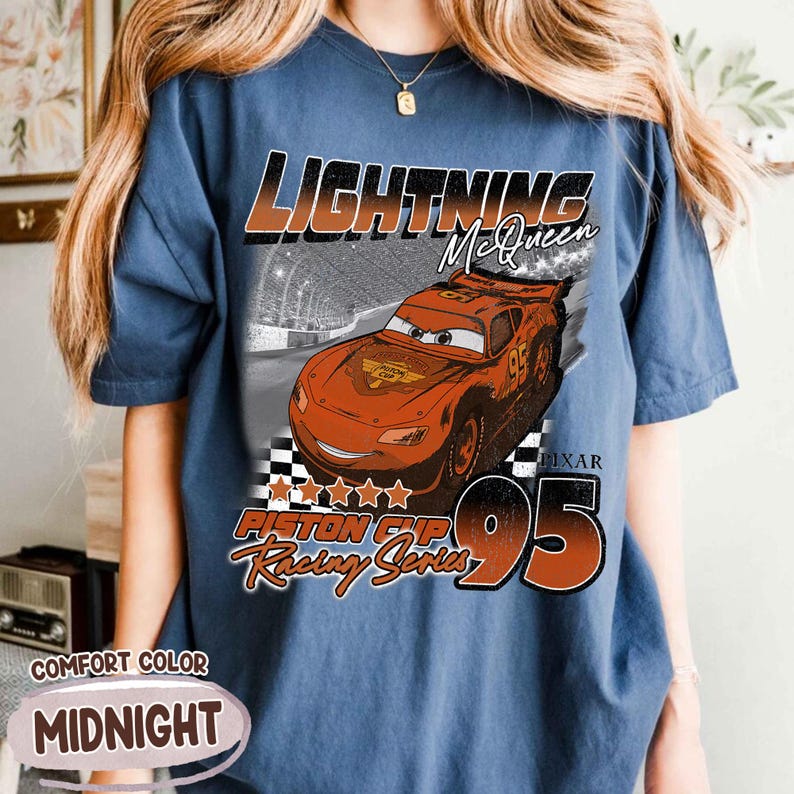 May include: Midnight blue t-shirt featuring Lightning McQueen from the Pixar Cars movie. The graphic includes the text "Lightning McQueen", "Piston Cup Racing Series", and the number "95". The shirt is labeled "Comfort Color".