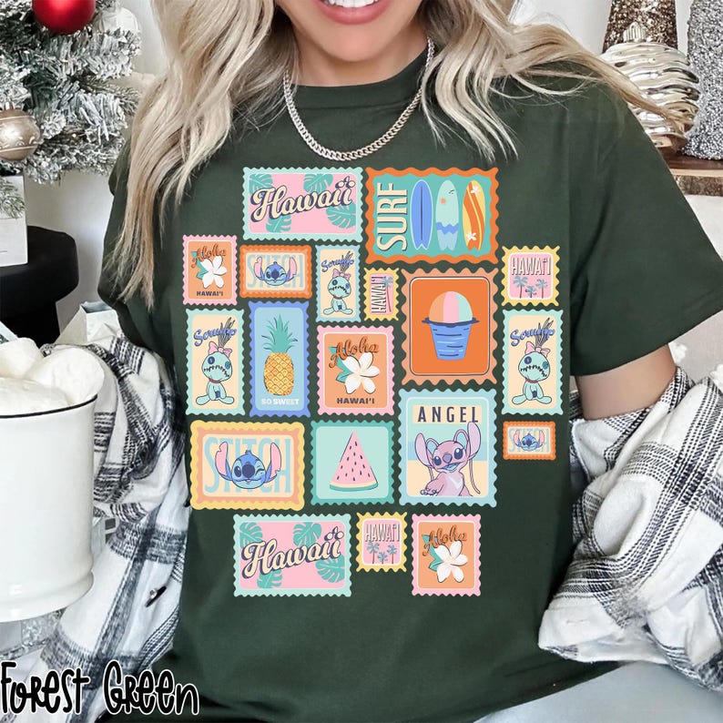 May include: Forest green t-shirt featuring a collage of colorful postage stamp designs with Hawaiian themes. Stamps include images of surfboards, pineapples, flowers, and the character Stitch. The word "Hawaii" is printed on several stamps.