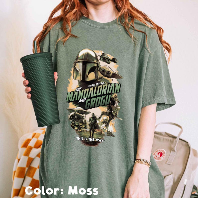 Puede incluir: Una camiseta verde musgo con un gr&aacute;fico de la serie Star Wars, "The Mandalorian and Grogu". El dise&ntilde;o incluye im&aacute;genes del Mandaloriano, Grogu y otros personajes, con la frase "This is the Way".