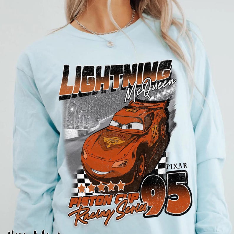 May include: Light blue long-sleeve shirt featuring Lightning McQueen from the movie Cars. The graphic includes the text "LIGHTNING McQueen", "PISTON CUP Racing Series", and the number "95". The design showcases the character in a race.