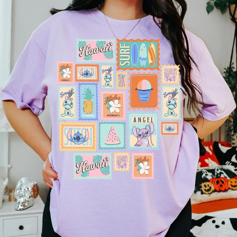 May include: A light purple t-shirt featuring a collage of colorful postage stamp designs with Hawaiian themes. The stamps include images of Stitch, pineapples, surfboards, and the word "Hawaii".