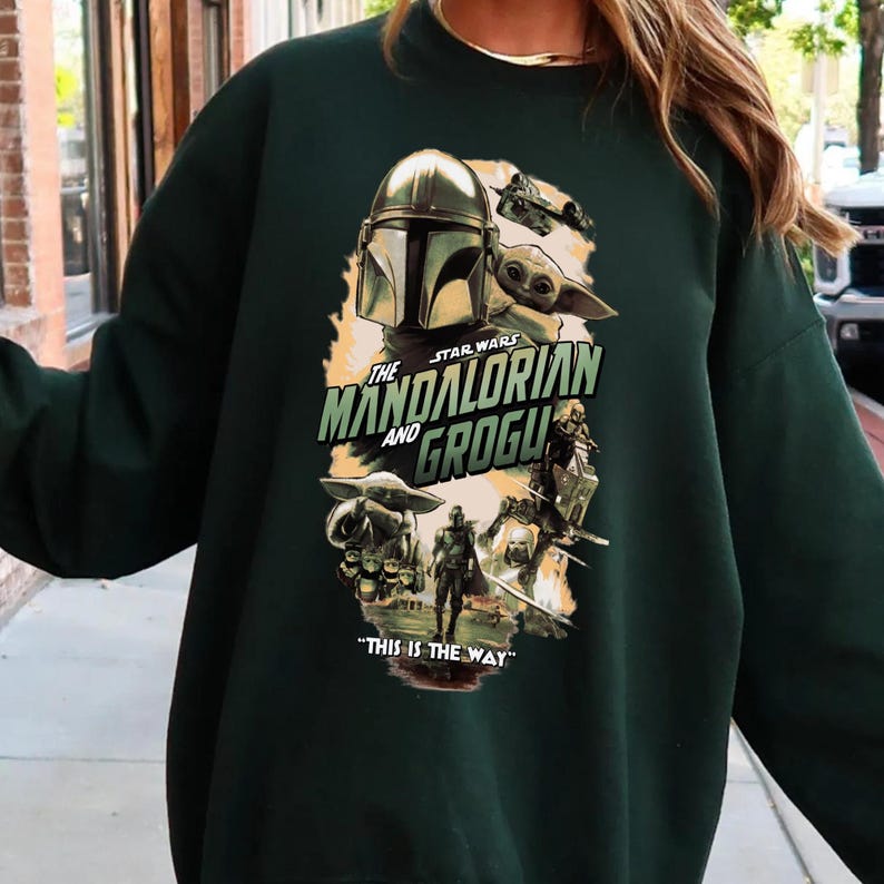 Puede incluir: Sudadera verde oscuro con un gr&aacute;fico de la serie Star Wars, "The Mandalorian and Grogu". El dise&ntilde;o incluye el casco del Mandaloriano, Grogu y la frase "This is the Way".