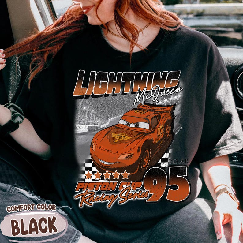 May include: Black t-shirt featuring Lightning McQueen from the movie Cars. The design includes the text "LIGHTNING McQueen", "Piston Cup Racing Series", and the number "95". The shirt is labeled "Comfort Color BLACK".