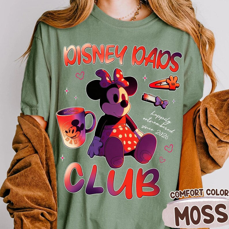 Może przedstawiać: Zielona koszulka w kolorze mchu z grafiką Myszki Minnie, kubkiem i napisem "Disney Dads Club". Projekt zawiera słowa "happily outnumbered since 2026". Koszulka jest oznaczona jako "Comfort Color" i "Moss".