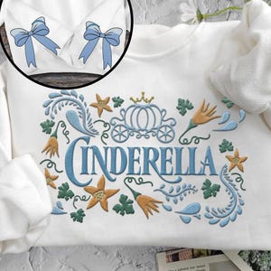 May include: White sweatshirt with a blue embroidered design of Cinderella's carriage, flowers, and the word "Cinderella".
