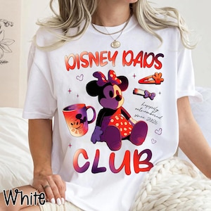Może przedstawiać: Biała koszulka z kolorową grafiką przedstawiającą Minnie Mouse, kubek do kawy oraz napisem "DISNEY DADS CLUB". Projekt zawiera frazę "happily outnumbered since 2026". Koszulka ma okrągły dekolt i kr&oacute;tkie rękawy.