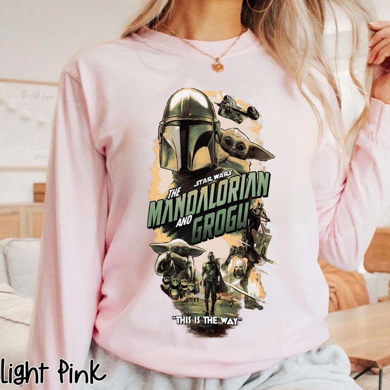 Puede incluir: Sudadera rosa claro de manga larga con un gr&aacute;fico de la serie Star Wars, "The Mandalorian and Grogu". El dise&ntilde;o incluye el casco del Mandaloriano, Grogu y la frase "This is the Way."