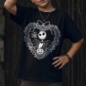 May include: Black t-shirt with a white graphic of Jack Skellington from "The Nightmare Before Christmas." The design includes a heart-shaped frame, bow, and a pumpkin. The text "The Nightmare Before Christmas" is also visible.