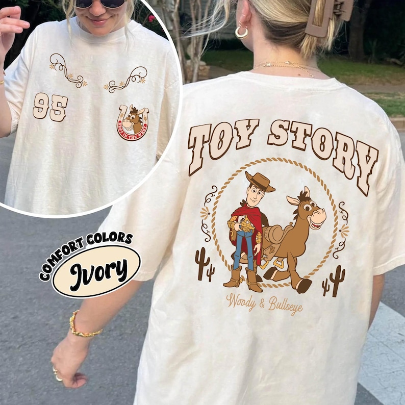 May include: Ivory-colored t-shirt featuring a "Toy Story" design on the back with Woody and Bullseye. The front has the number "95" and decorative elements. The shirt is labeled "Comfort Colors" and "Ivory".