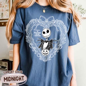 May include: Midnight blue Comfort Colors t-shirt with a white graphic of Jack Skellington from The Nightmare Before Christmas. The design includes a wreath, a pumpkin, and the movie title. The shirt has short sleeves.