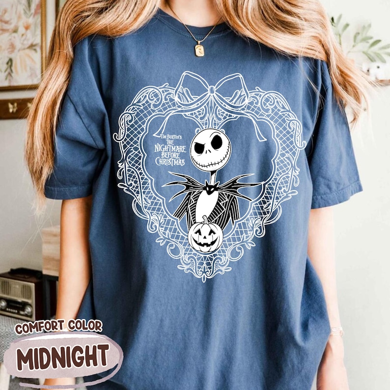 May include: Midnight blue Comfort Colors t-shirt with a white graphic of Jack Skellington from The Nightmare Before Christmas. The design includes a wreath, a pumpkin, and the movie title. The shirt has short sleeves.