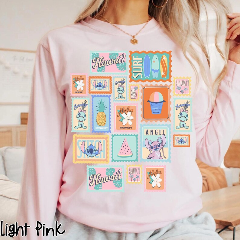 May include: Light pink long-sleeve sweatshirt featuring a colorful collage of Hawaiian-themed postage stamps. The stamps include images of Stitch, pineapples, surfboards, and the word "Hawaii". The text "Light Pink" is at the bottom.