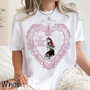 May include: White t-shirt with a pink heart-shaped frame and a bow, featuring the text "The Nightmare Before Christmas." Inside the frame is a cartoon illustration of Sally. The word "White" is printed at the bottom left of the t-shirt.