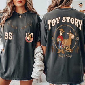 May include: Dark gray t-shirts with a Toy Story theme. The front features the number 95 and a horseshoe with a cartoon horse. The back displays Woody and Bullseye with the words "Toy Story".