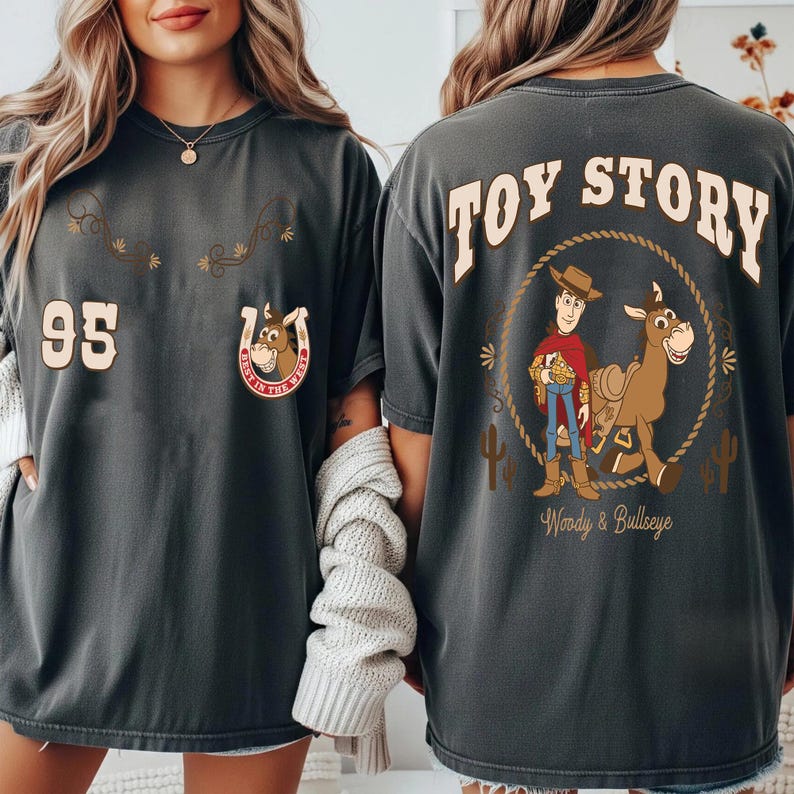 May include: Dark gray t-shirts with a Toy Story theme. The front features the number 95 and a horseshoe with a cartoon horse. The back displays Woody and Bullseye with the words "Toy Story".