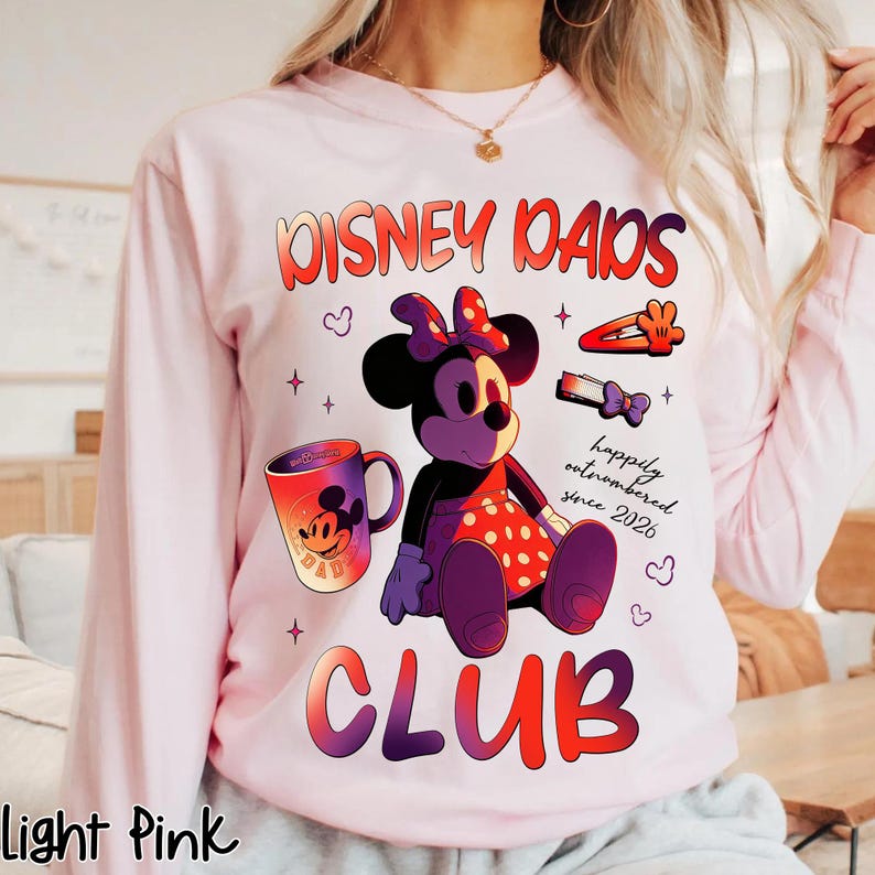 Może przedstawiać: Jasnor&oacute;żowa bluza z długim rękawem z motywem Myszki Minnie. Projekt zawiera napisy "Disney Dads Club", ilustrację Myszki Minnie, kubek i spinki do włos&oacute;w. Tekst "happily outnumbered since 2026" jest r&oacute;wnież zawarty.