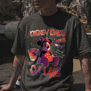 Może przedstawiać: Ciemnoszara koszulka z grafiką Myszki Minnie i napisem "Disney Dads Club". Projekt zawiera kubek, spinkę do włos&oacute;w i frazę "happily outnumbered since 2026."