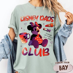Może przedstawiać: Jasnozielona koszulka Comfort Color z grafiką przedstawiającą Minnie Mouse, kubek oraz napisem "Disney Dads Club" i "happily outnumbered since 2026". Koszulka ma r&oacute;wnież etykietę "Comfort Color Bay".