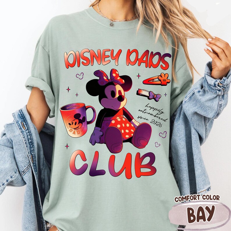 Może przedstawiać: Jasnozielona koszulka Comfort Color z grafiką przedstawiającą Minnie Mouse, kubek oraz napisem "Disney Dads Club" i "happily outnumbered since 2026". Koszulka ma r&oacute;wnież etykietę "Comfort Color Bay".