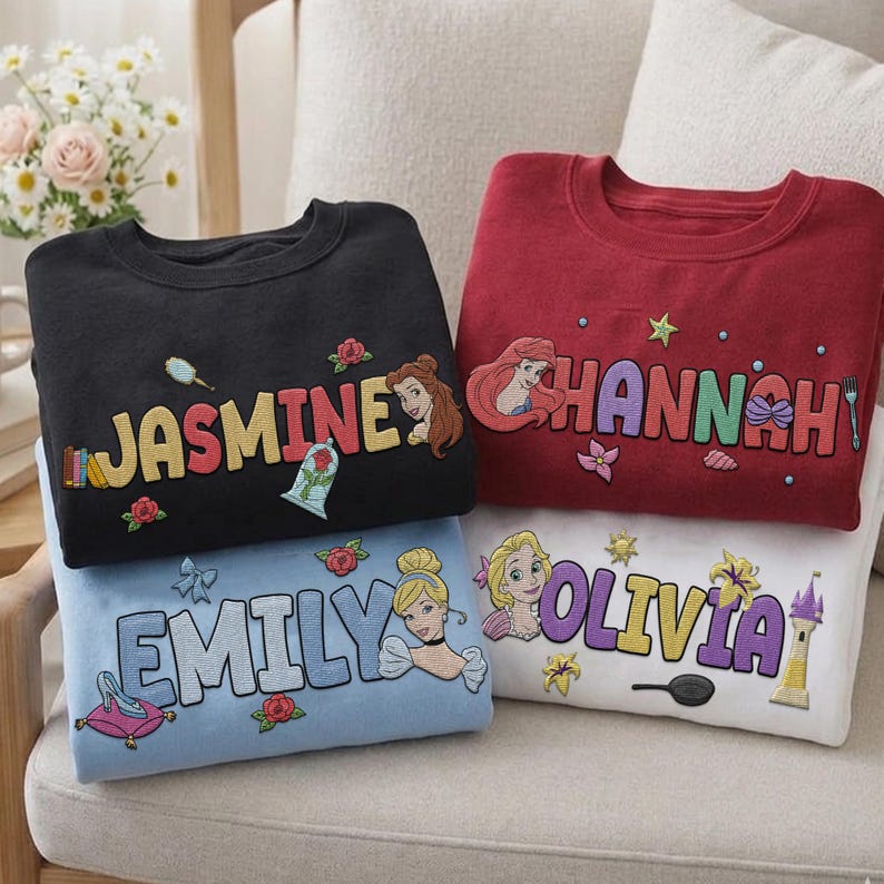 Puede incluir: Cuatro sudaderas en negro, rojo, azul claro y blanco, cada una bordada con un nombre y un gr&aacute;fico de princesa. La sudadera negra dice "JASMINE" con una princesa e iconos relacionados. La sudadera roja dice "HANNAH" con una princesa. La sudadera azul claro dice "EMILY" con una princesa. La sudadera blanca dice "OLIVIA" con una princesa.