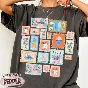 May include: Dark grey Comfort Color t-shirt with a collage of colorful Hawaiian-themed postage stamp designs. The stamps feature images of Stitch, pineapples, surfboards, flowers, and the word "Hawaii". The shirt is labeled "Pepper".