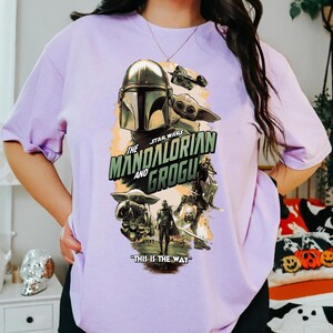 Puede incluir: Una camiseta de color lila claro con un dise&ntilde;o gr&aacute;fico de la serie Star Wars, "The Mandalorian and Grogu". El dise&ntilde;o incluye im&aacute;genes de The Mandalorian, Grogu y otros personajes, con la frase "THIS IS THE WAY."