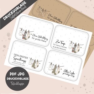 Puede incluir: Etiquetas imprimibles con temática de bebé. Las etiquetas presentan ilustraciones de calcetines colgados en un tendedero, con texto en alemán. Las etiquetas tienen forma rectangular con esquinas redondeadas. El fondo es de color beige claro.