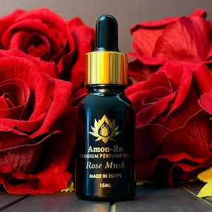 May include: A black glass bottle with a gold lid and dropper. The bottle is labeled "Amon-Ra Premium Perfume Oils Rose Musk Made in Egypt 15ML". The bottle is surrounded by red roses.