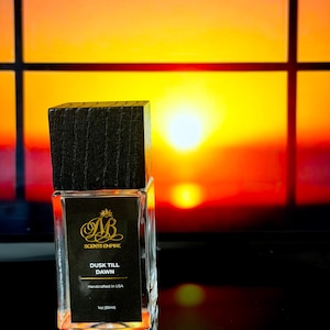 May include: A rectangular glass perfume bottle with a dark wooden cap. The label reads "SCENTS EMPIRE" and "DUSK TILL DAWN". The bottle contains 1 fl oz (30ml) of liquid and is handcrafted in the USA. The background is a sunset.