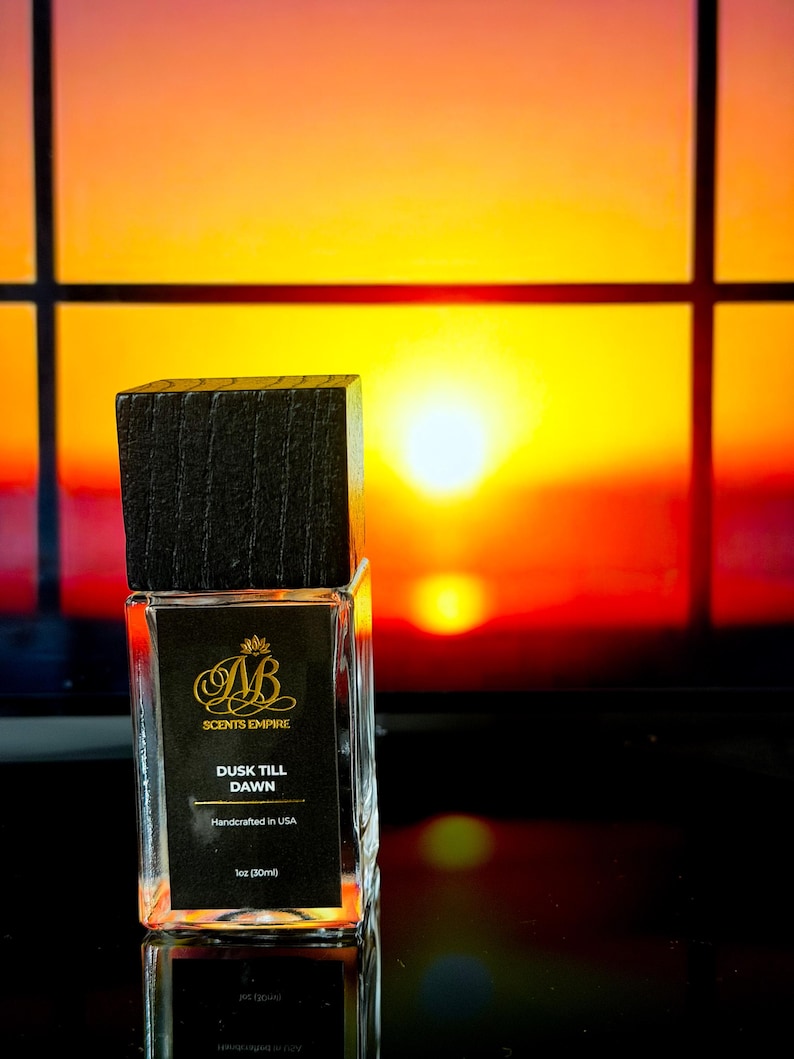 May include: A rectangular glass perfume bottle with a dark wooden cap. The label reads "SCENTS EMPIRE" and "DUSK TILL DAWN". The bottle contains 1 fl oz (30ml) of liquid and is handcrafted in the USA. The background is a sunset.