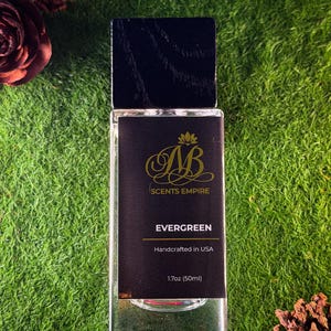 K&ouml;nnte beinhalten: Ein rechteckiger Glasparf&uuml;mflakon mit schwarzem Holzdeckel und schwarzem Etikett. Das Etikett zeigt ein goldenes Logo, den Text SCENTS EMPIRE, EVERGREEN, Handcrafted in USA und 50ml (1.7oz). Der Flakon ist durchsichtig und zeigt die Fl&uuml;ssigkeit.