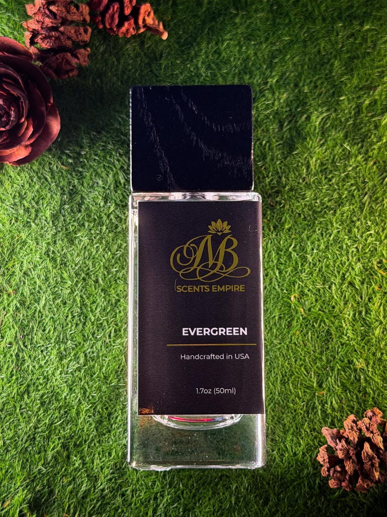 K&ouml;nnte beinhalten: Ein rechteckiger Glasparf&uuml;mflakon mit schwarzem Holzdeckel und schwarzem Etikett. Das Etikett zeigt ein goldenes Logo, den Text SCENTS EMPIRE, EVERGREEN, Handcrafted in USA und 50ml (1.7oz). Der Flakon ist durchsichtig und zeigt die Fl&uuml;ssigkeit.