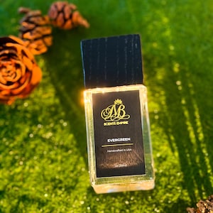 K&ouml;nnte beinhalten: Ein rechteckiger Glasparf&uuml;mflakon mit einem schwarzen Holzdeckel. Das schwarze Etikett zeigt das goldene Logo AB SCENTS EMPIRE, den Text EVERGREEN, Handcrafted in USA und 1oz (30ml). Der Flakon ist durchsichtig und zeigt die Fl&uuml;ssigkeit.